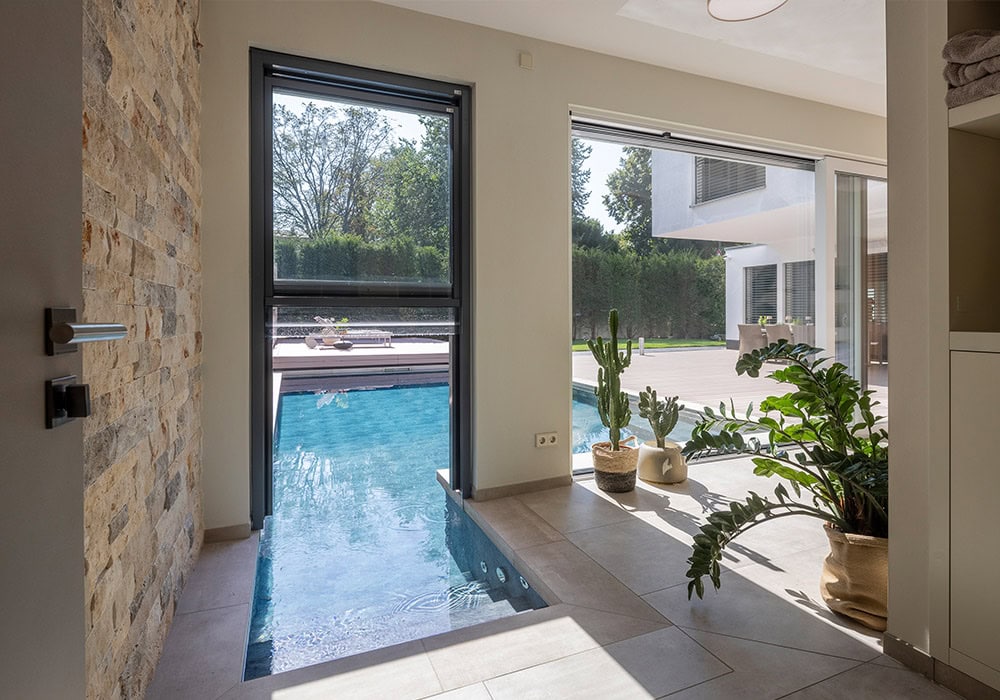 Ein moderner Wohnraum mit Pool, Pflanzen und großer Fensterfront mit Blick nach draußen.