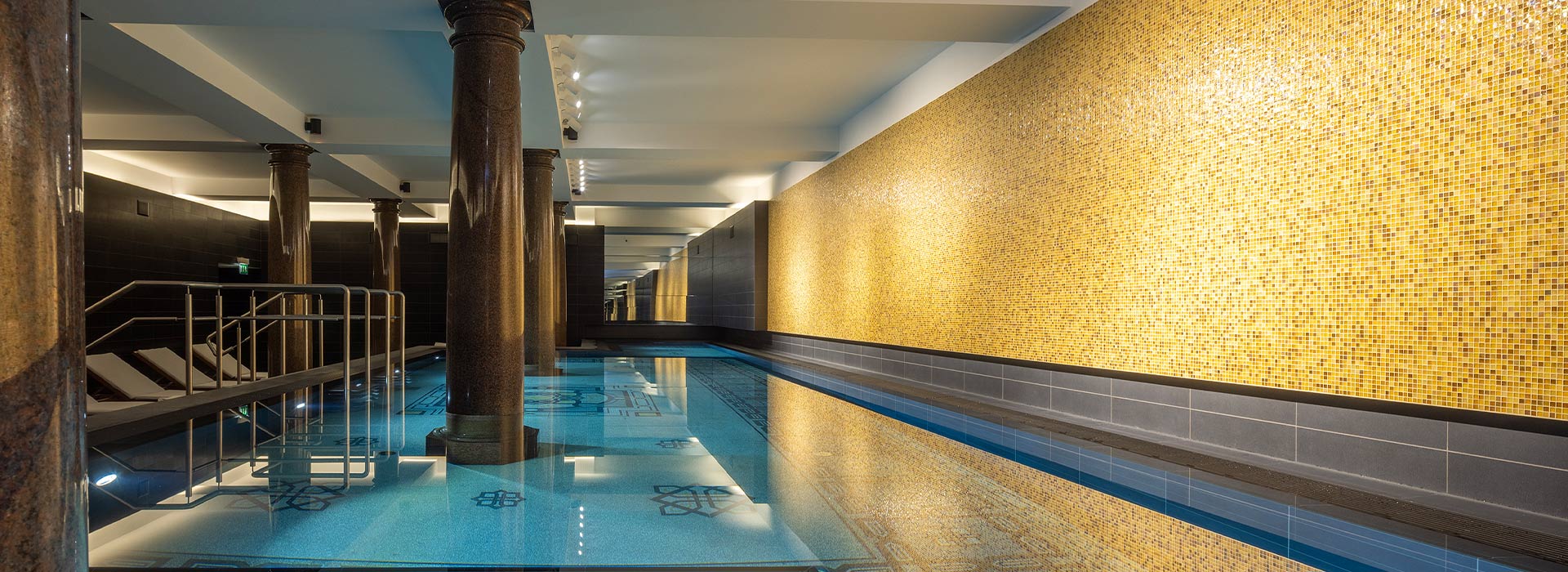 Ein luxuriöser Innenpool mit goldener Mosaikwand und eleganten Säulen, stilvolle Atmosphäre.