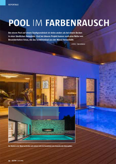 Moderner Pool bei Nacht, beleuchtet in Blau, mit angrenzendem, stilvollem Gebäude und Steinwand.
